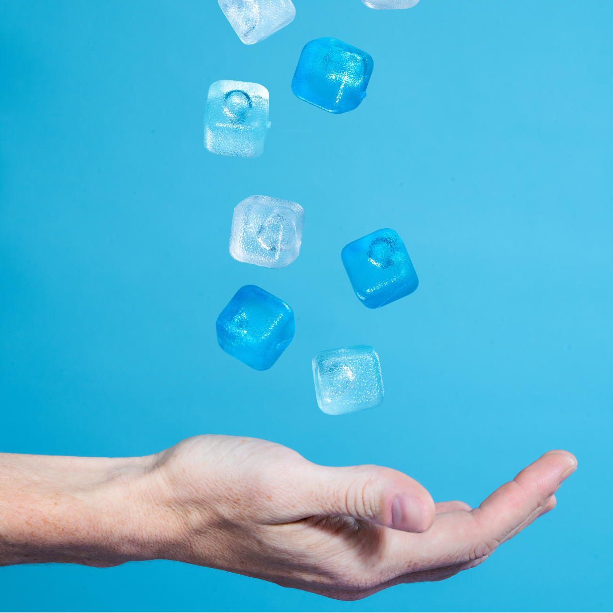 Hand catching floating ice cubes against a blue background