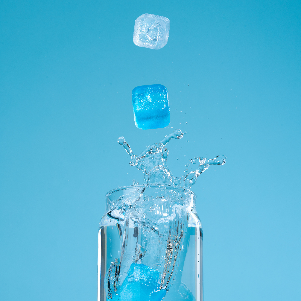 Blue ice cubes being dropped into a glass with a blue background