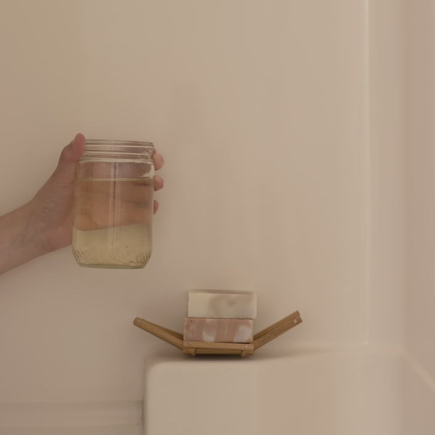 Hand holding a jar over a soap dish with soap on a beige surface