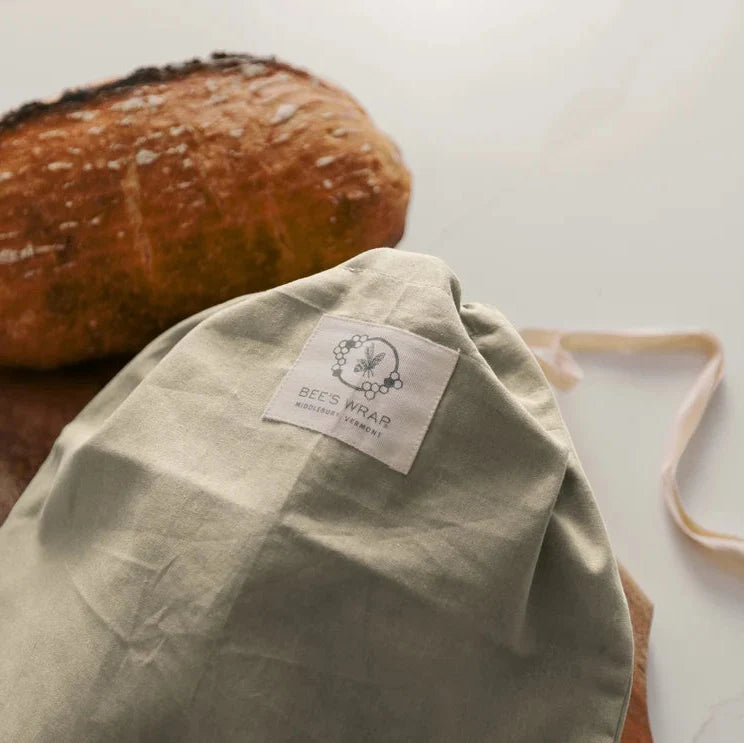 Beige drawstring bag with a label next to a loaf of bread on a wooden board.