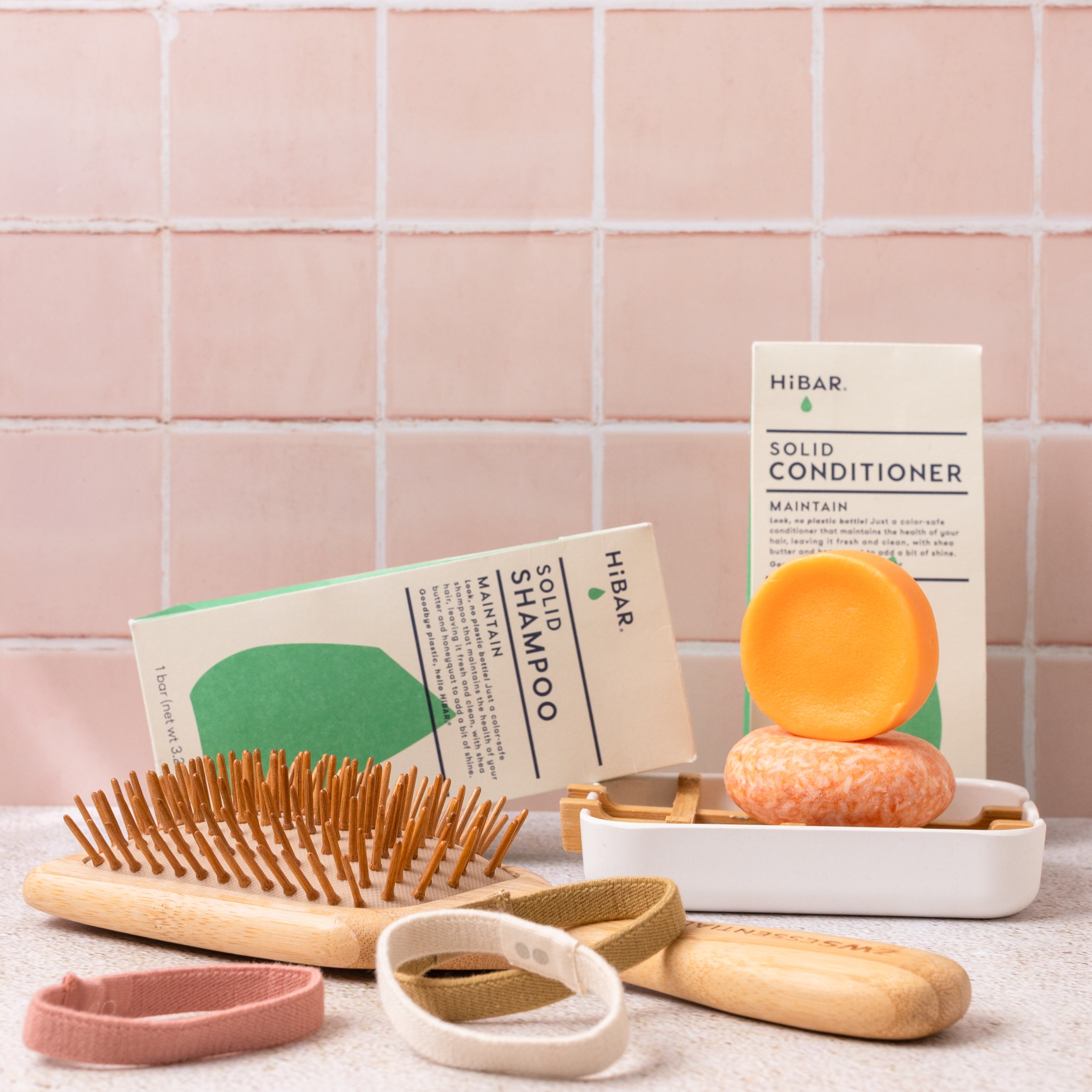 Bath products including a shampoo bar, conditioner bar, and hairbrush on a tiled bathroom floor.