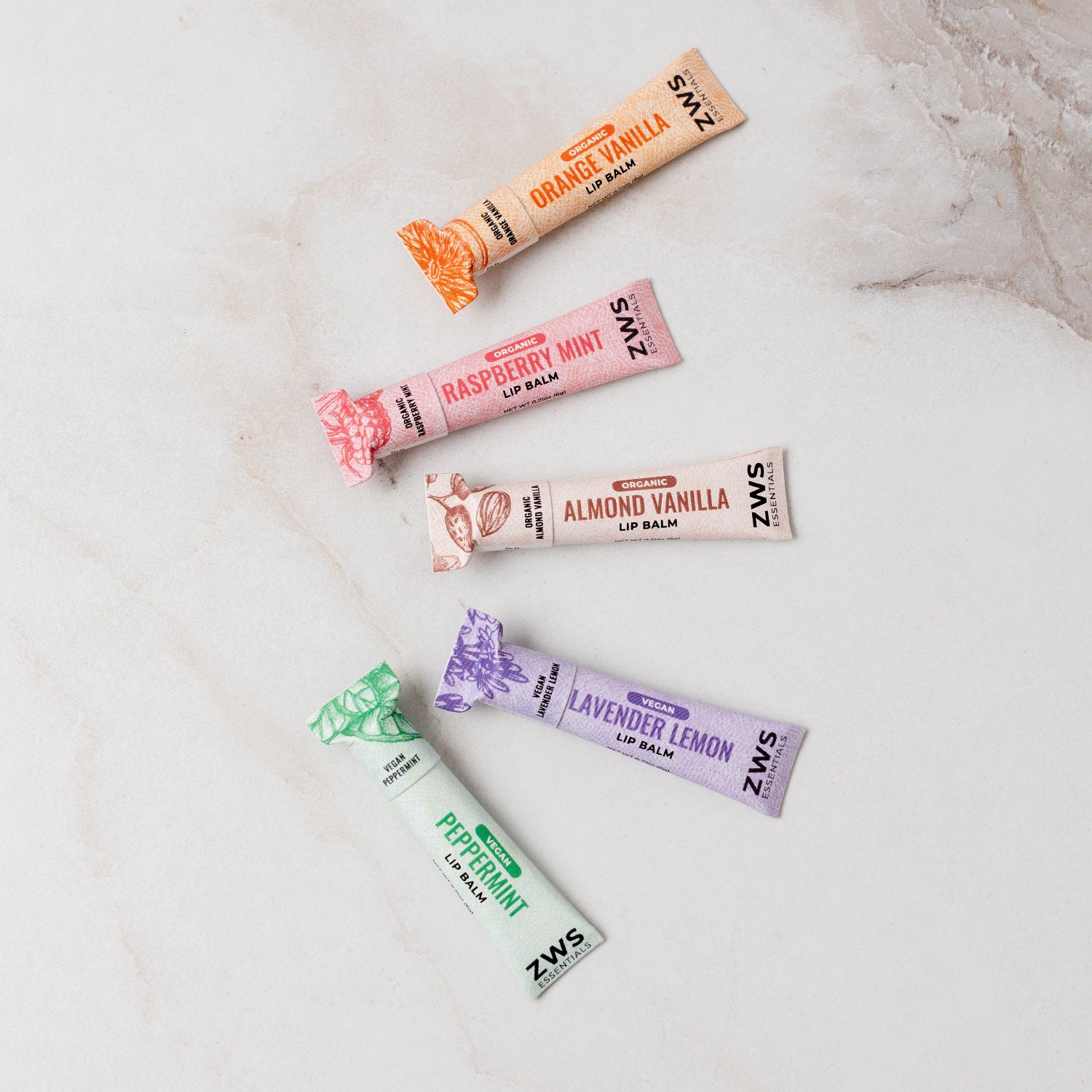 Five ZWS lip balm tubes in various flavors on a marble surface