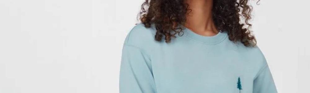image of a person with long hair wearing a light blue crewneck sweatshirt with a tree logo on it