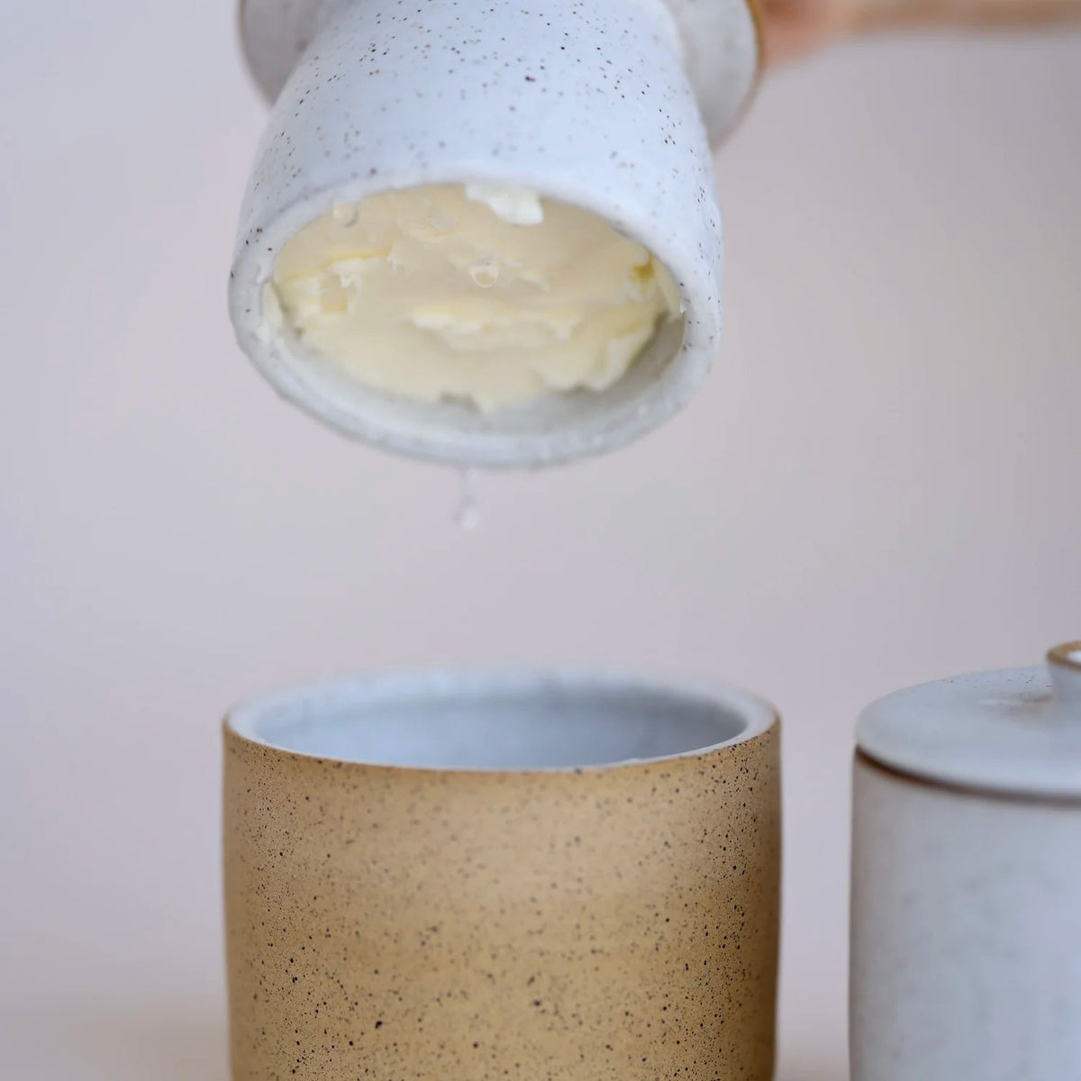 Ceramic containers with a hand holding one, on a plain background