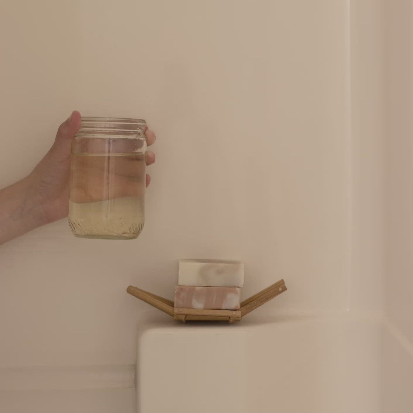 Hand holding a jar over a soap dish with soap on a beige surface