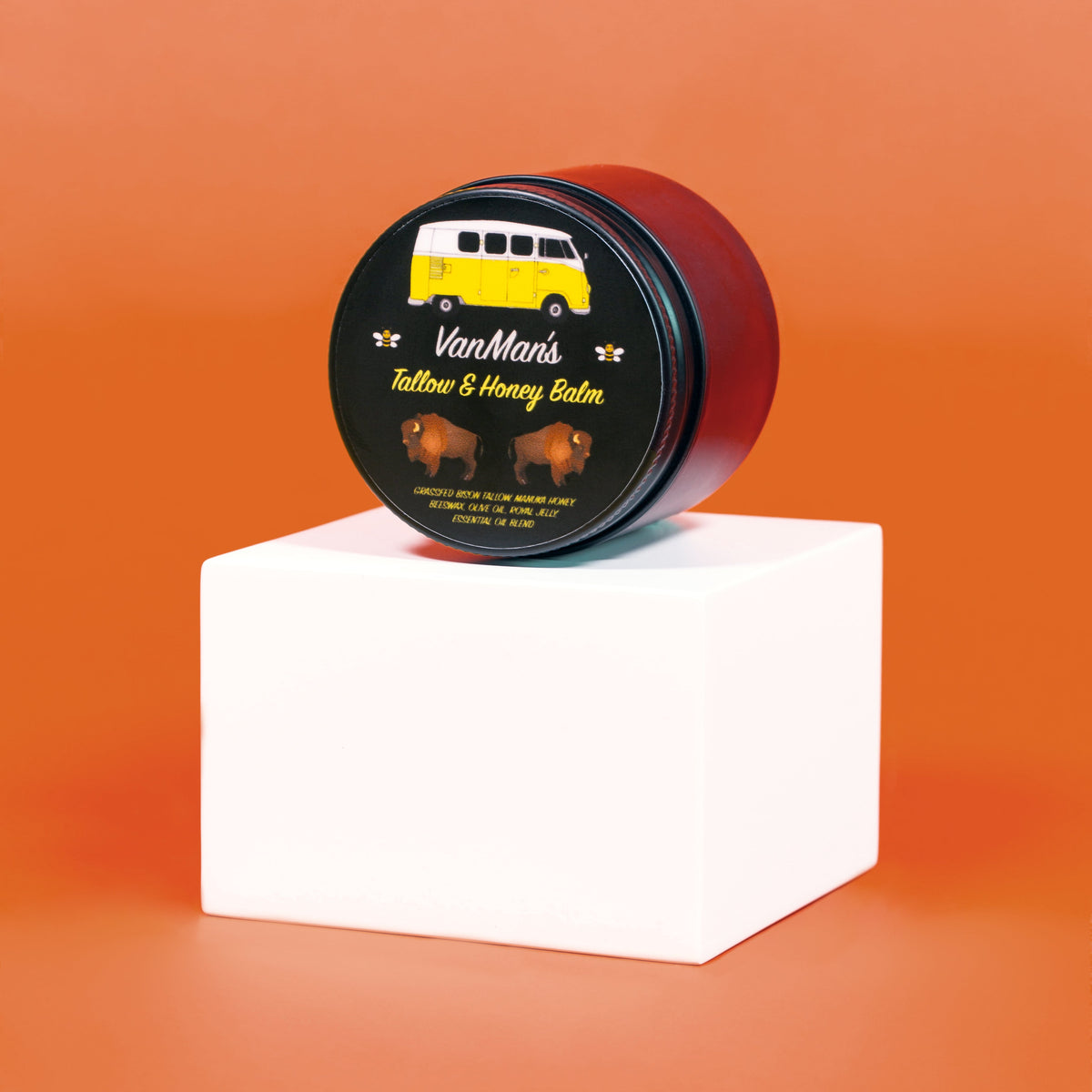 Van Marm's Tattoo & Honey Balm jar on a white block with an orange background