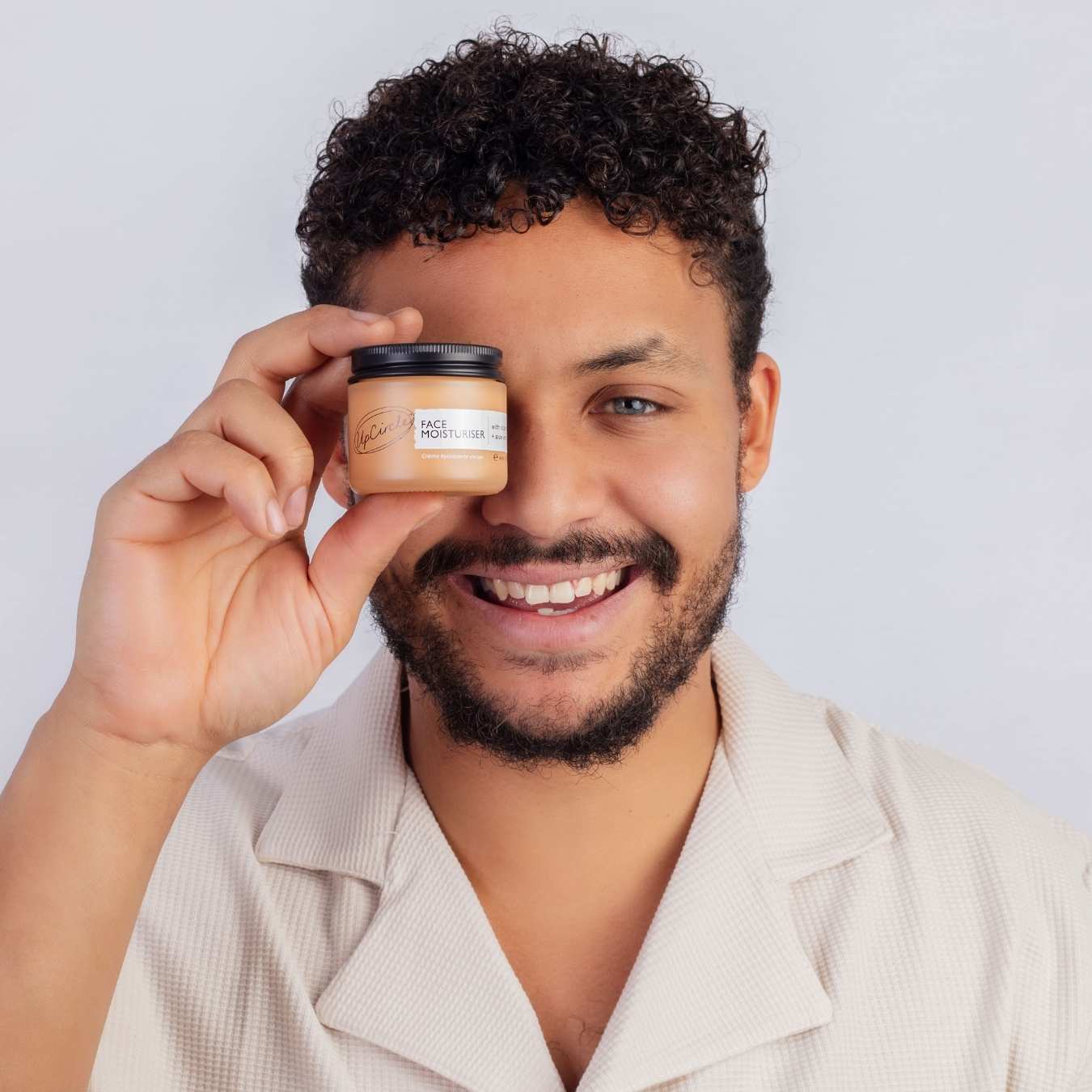 Man holding a jar of hair product in front of his face against a plain background