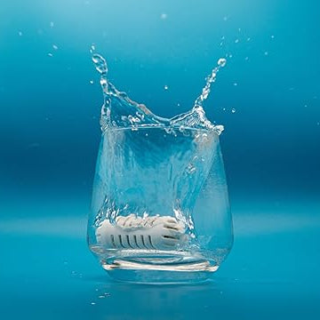 Clear glass with a white object inside, splashing water against a blue background