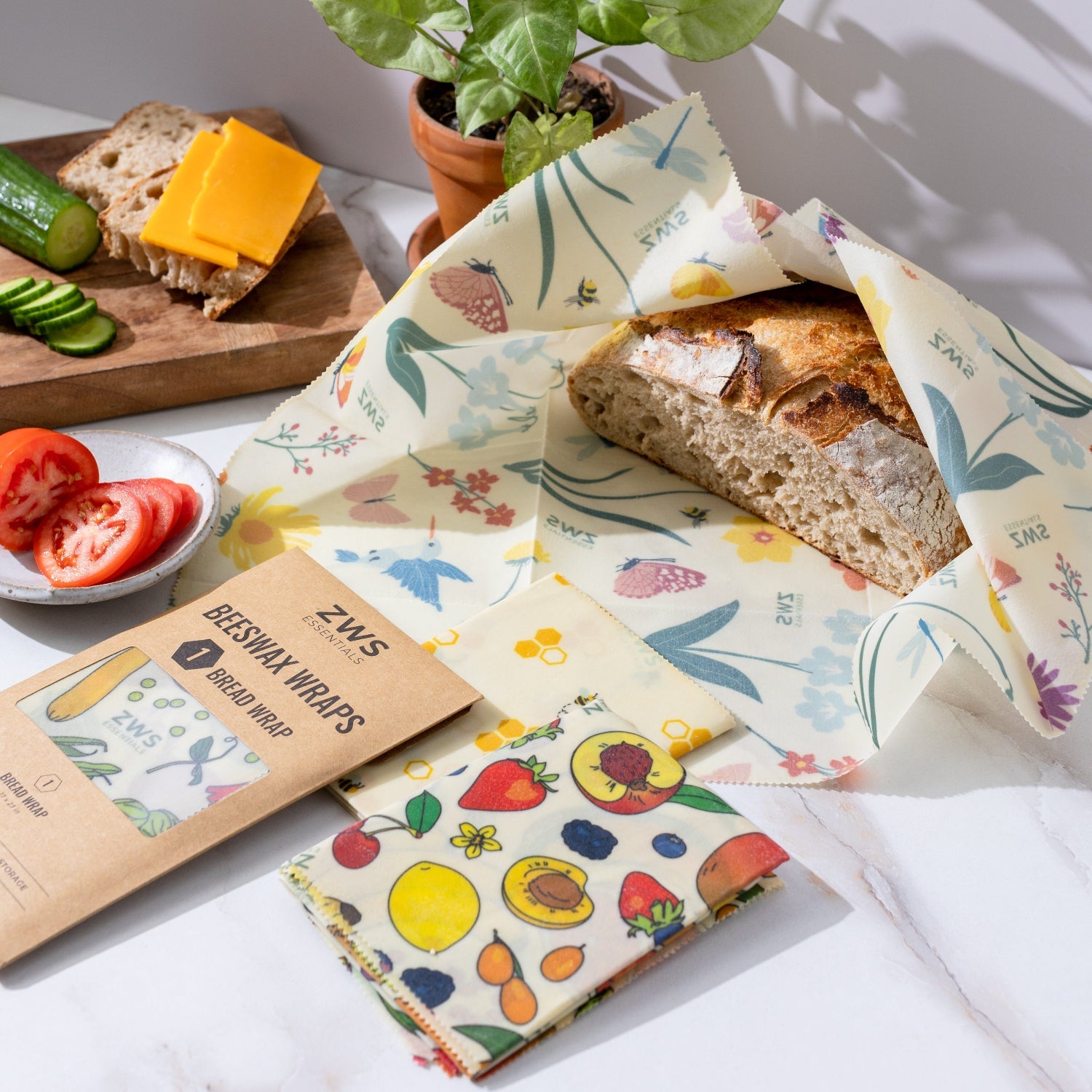 Reusable paper wraps with colorful designs on a white surface with a plant in the background.