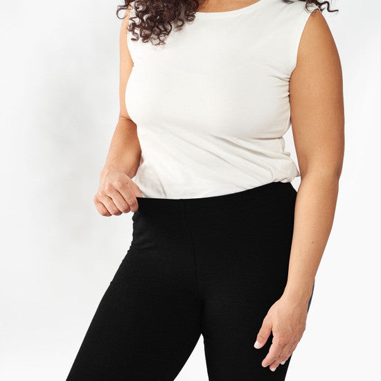 Person wearing a white sleeveless top and black pants on a plain background