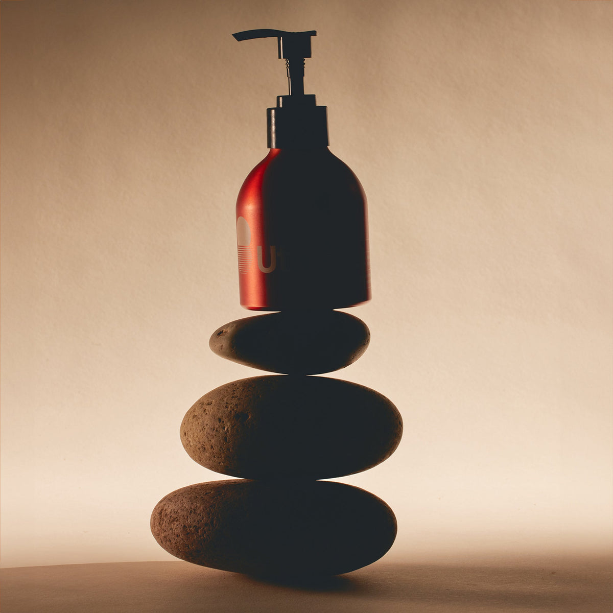 Bottle with pump on stacked stones against a beige background