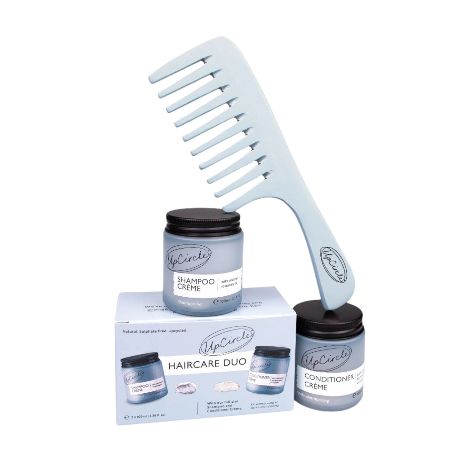 A blue bamboo wide tooth comb alongside two glass jars of UpCircle shampoo and conditioner, with the brand's packaging boxes.