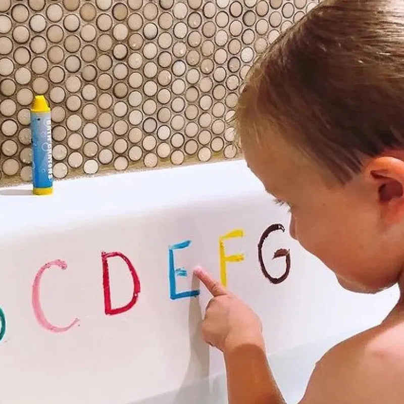 Child writing letters in the bathtub with colorful bath crayons.