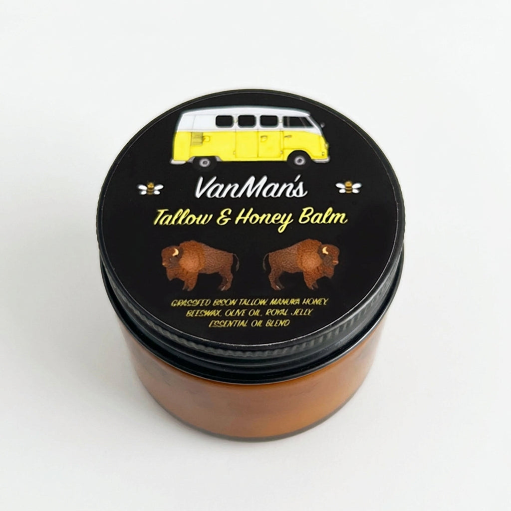 A round tin of Van Man's Tallow & Honey Balm with a black lid featuring a yellow van illustration and bison graphics, set against a warm peach background with diagonal shadows.