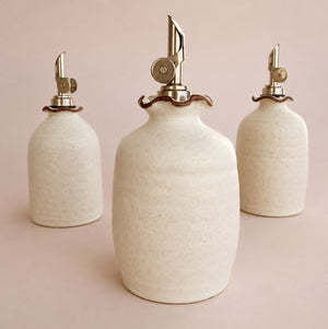 Three ceramic siphon bottles with metal nozzles on a pink background