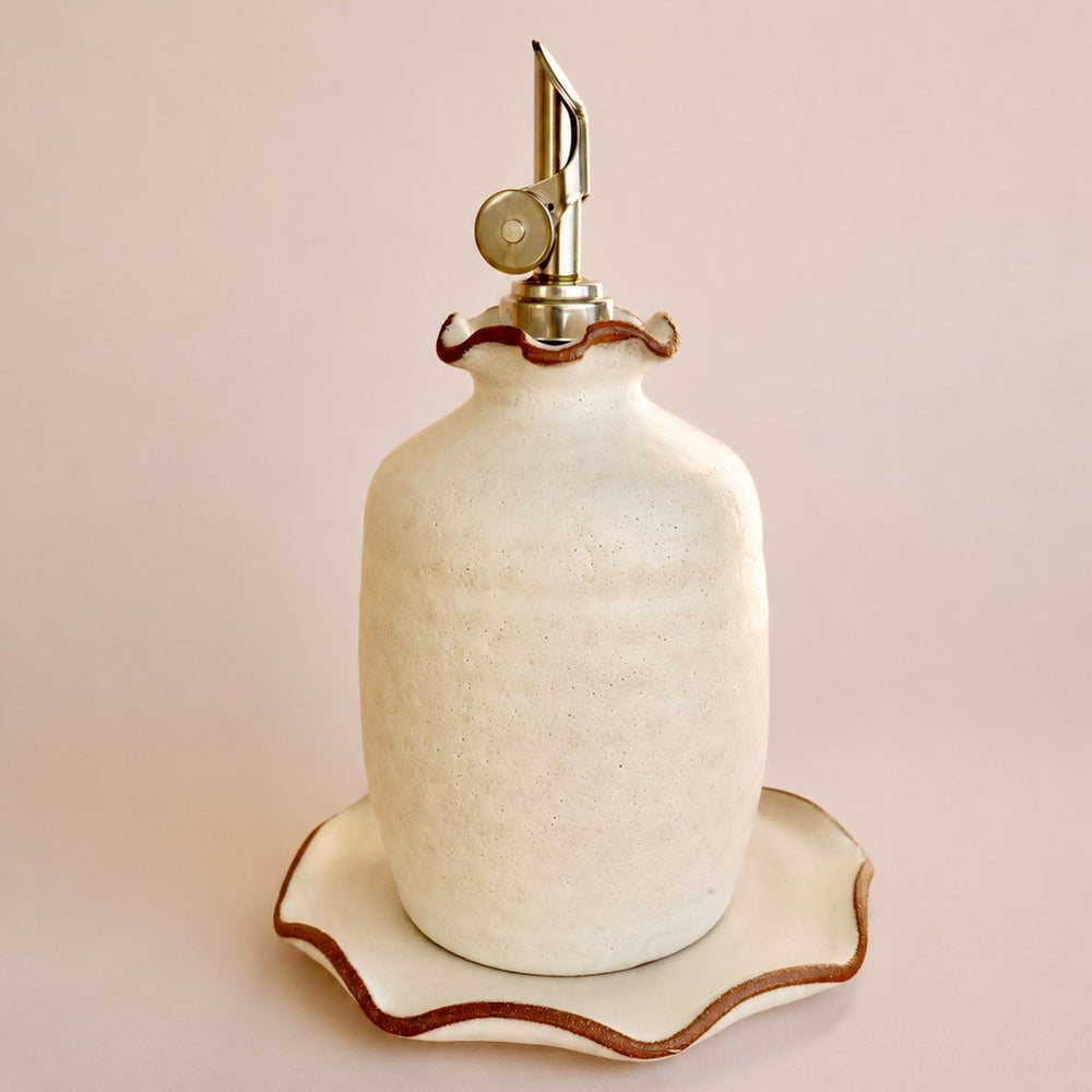 Decorative ceramic bottle with scalloped edge on a matching stand against a light pink background