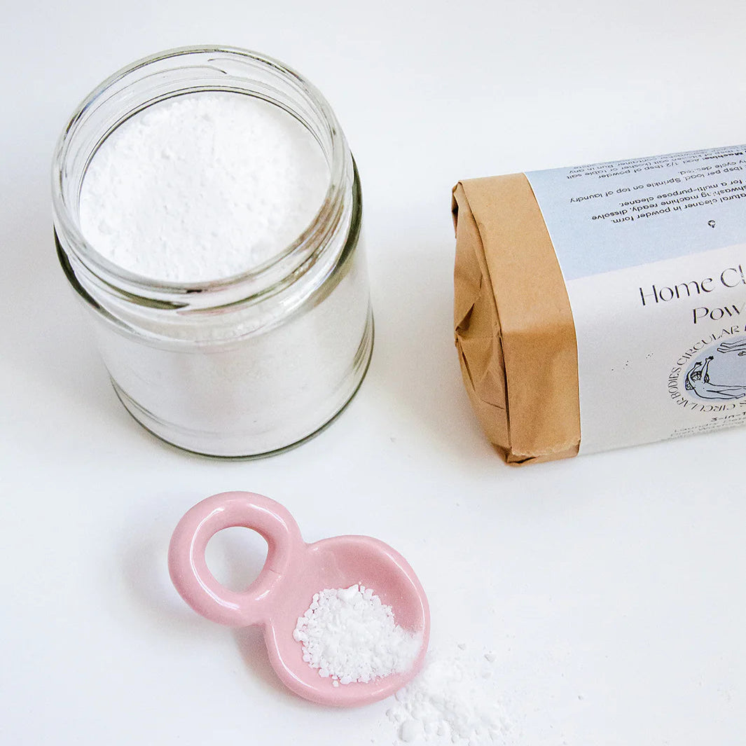 Glass jar of powder with a pink scoop and packaging on a white background